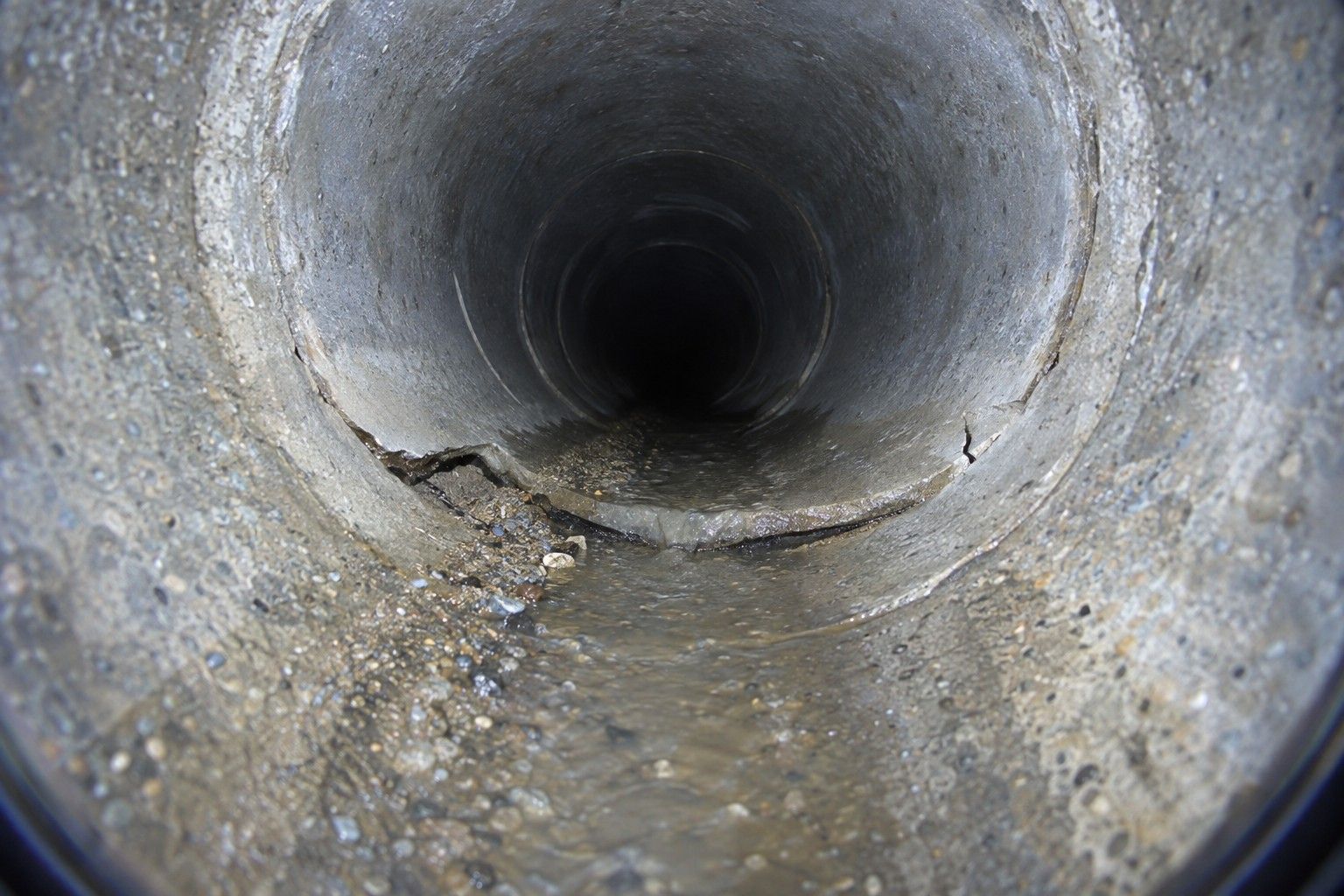 Joint déboîté entre deux tuyaux en béton, avec une fissure et du dépôt, vu par la caméra