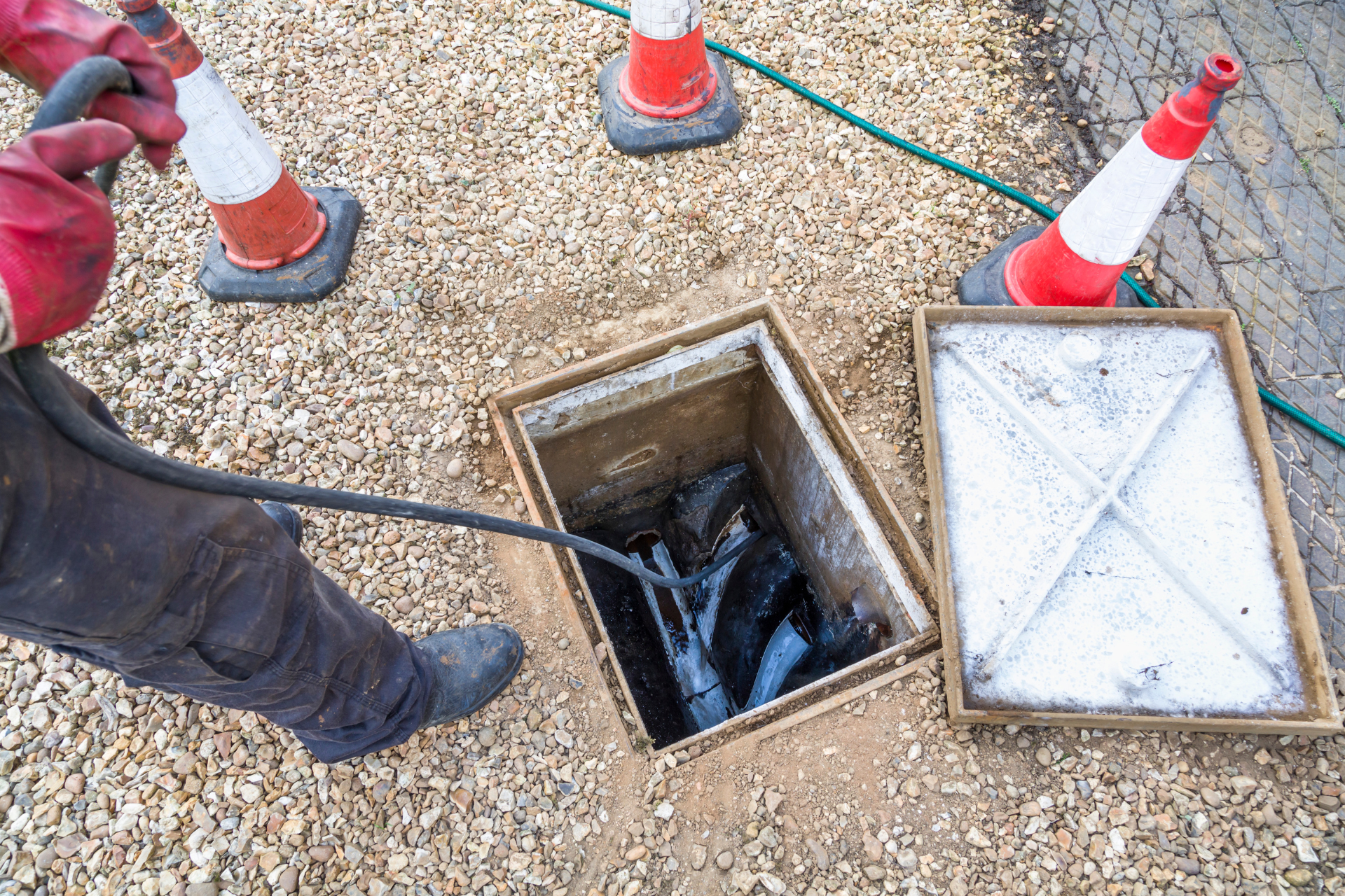 Homme débloquant une canalisation d'eaux usées par une chambre d'inspection ouverte